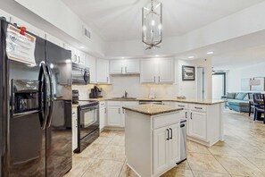 A modern kitchen with white cabinetry, a stainless steel refrigerator, a built-in oven, and a central island with a granite countertop. - Gorgeous beachfront condo with open layout, pools, tennis, & gym (Orange Beach)