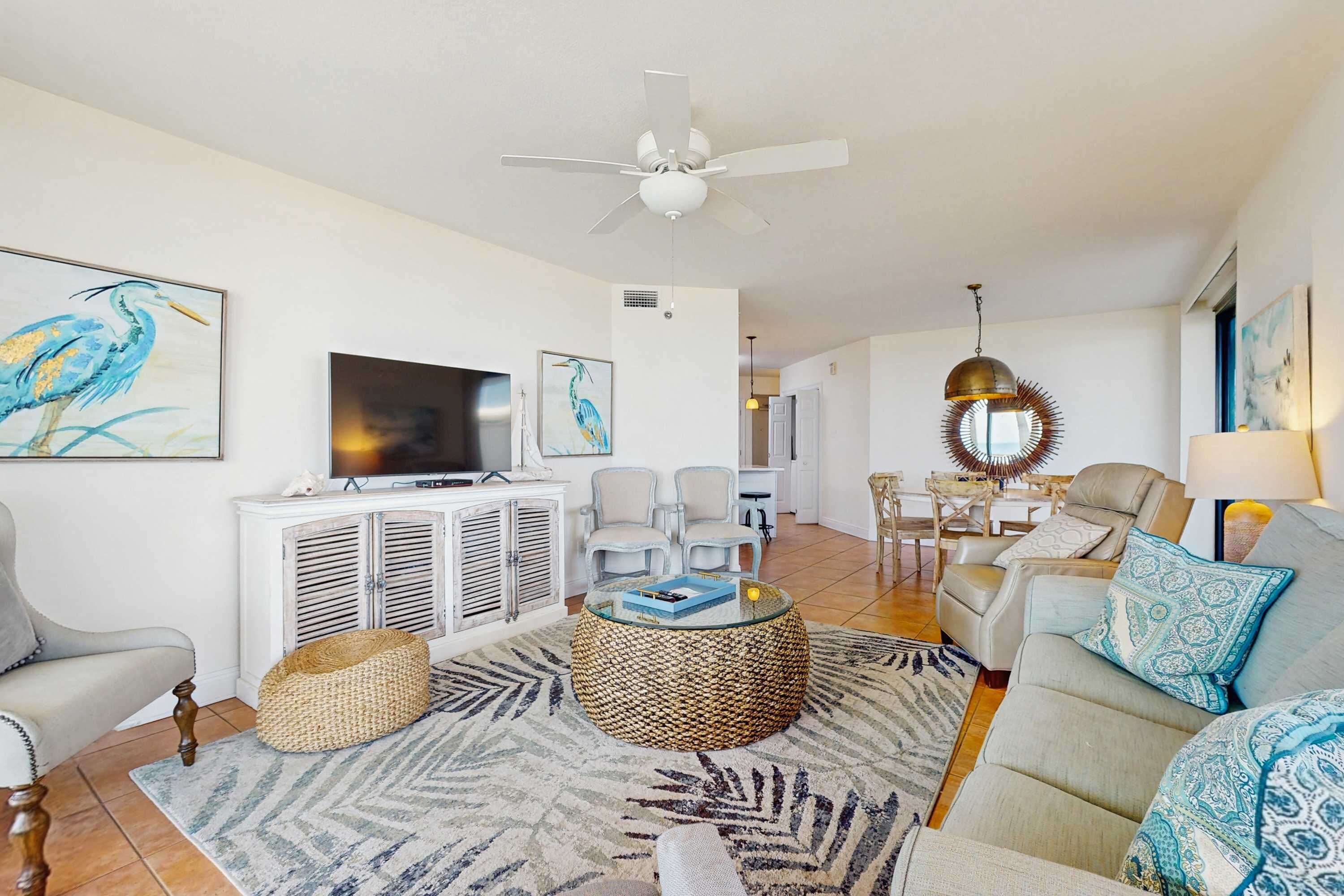 A living room with a ceiling fan, a television, a sofa, a coffee table, and a dining area with chairs.