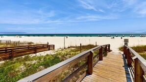 A wooden boardwalk leading to a sandy beach with a clear sky. - Stunning Gulf front condo w/ a spacious layout, shared pools, & fitness room (Orange Beach)