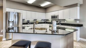 Una cocina moderna con armarios blancos, electrodomésticos de acero inoxidable, una encimera de granito negro y una isla central con asientos.