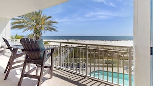 Een balkon met uitzicht op het strand, een zwembad en buitenmeubels.