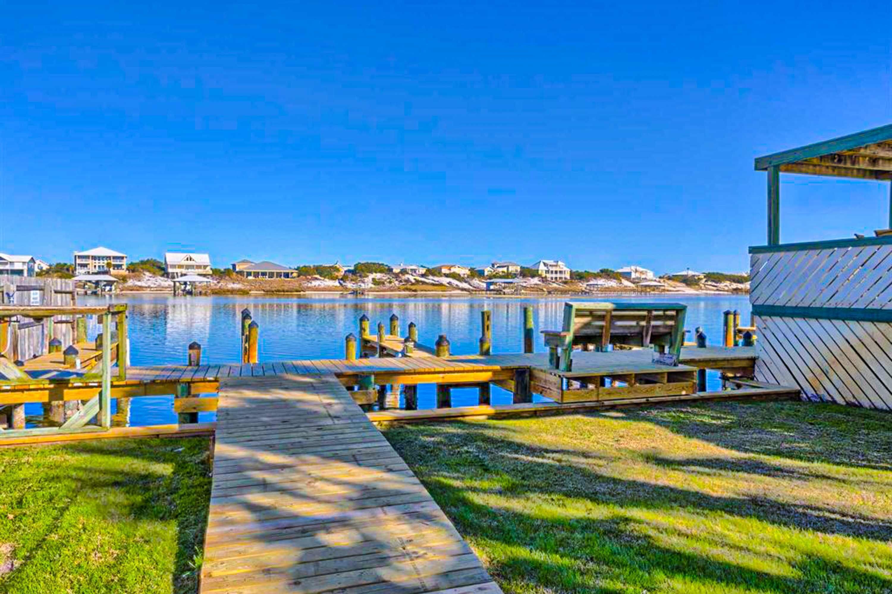 A wooden dock leading to a pier with a covered seating area and a building with a sloped roof.