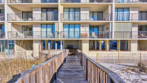 Un hotel de varios pisos con balcones, un paseo marítimo de madera y vistas a la playa.