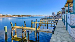 Un muelle de madera se adentra en aguas tranquilas, con un edificio con balcones a la derecha.