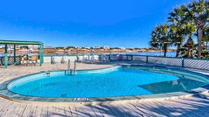 Una piscina circular con muelle de madera, sillas de descanso y vista al océano.