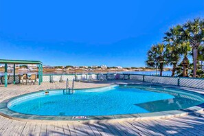 Ein runder Pool mit Holzterrasse, Liegestühlen und Blick auf den Ozean.