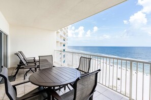 A balcony with a table and chairs, overlooking a beach with a clear view of the ocean. - Beachfront condo with amazing views overlooking the Gulf of America featuring resort style pools. (Orange Beach)