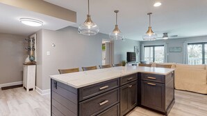 Uma cozinha moderna com armários escuros, bancada de mármore e iluminação pendente.