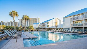 Piscina com espreguiçadeiras, palmeiras e um edifício alto ao fundo.