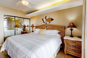 A bedroom with a large bed, a headboard with a decorative fish, a mirror, bedside tables with lamps, and a ceiling fan. - Gulf-front getaway with pool, hot tub, athletic courts & central AC (Orange Beach)