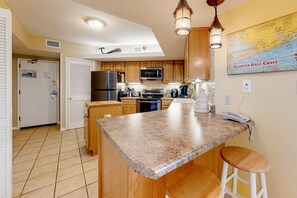 A kitchen with granite countertops, wooden cabinets, a refrigerator, microwave, stove, and a phone on the counter. - Gulf-front getaway with pool, hot tub, athletic courts & central AC (Orange Beach)