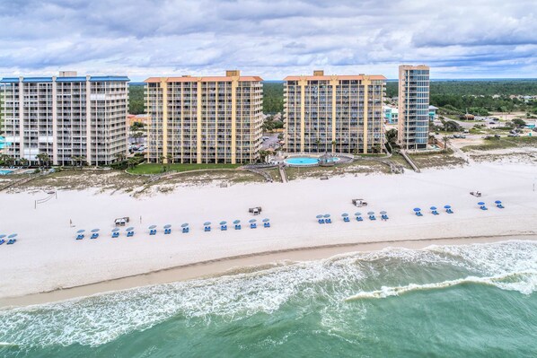 A beachfront hotel with multiple high-rise buildings, a sandy beach, and a pool area. - Gulf-front getaway with pool, hot tub, athletic courts & central AC (Orange Beach)