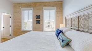 A bedroom with a large bed, wooden walls, two windows with blinds, and a decorative headboard. - Friendly home with private pool, WiFi, private washer,dryer, and central AC (Orange Beach)