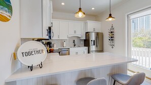 A modern kitchen with white cabinets, a central island with bar stools, pendant lighting, and a view of the outdoors. - Friendly home with private pool, WiFi, private washer,dryer, and central AC (Orange Beach)