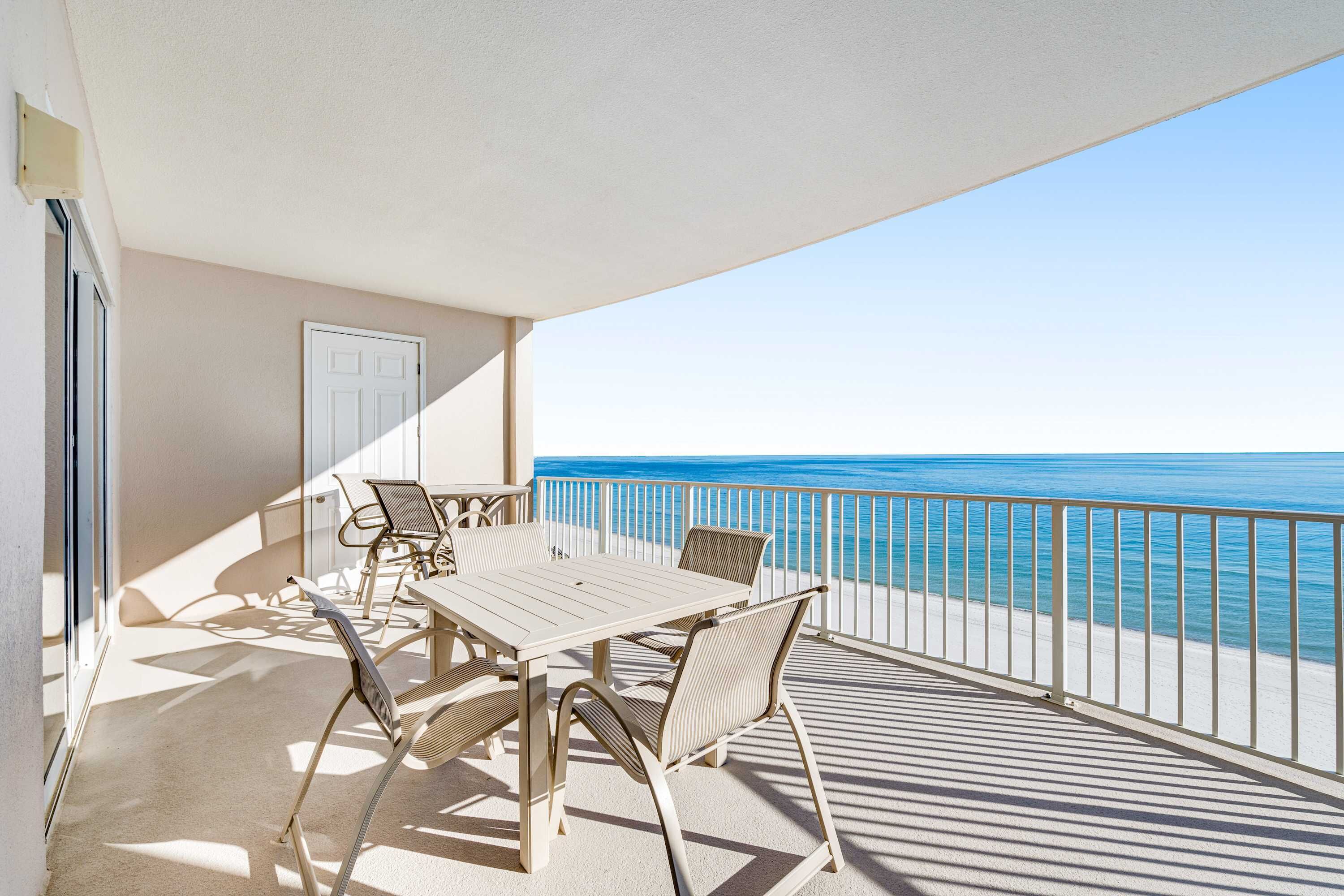 Een balkon met een tafel en stoelen, een witte deur en uitzicht op de oceaan.