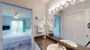 A hotel room with a bed, a bathroom with a sink and mirror, and a balcony with a TV. - Gulf-View Condo with Balcony, WiFi, Shared Pool & Gym - Steps from Beach (Orange Beach)