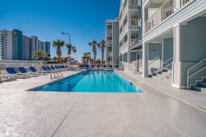 A swimming pool with lounge chairs, a staircase, and a view of tall buildings. - Gulf-View Condo with Balcony, WiFi, Shared Pool & Gym - Steps from Beach (Orange Beach)
