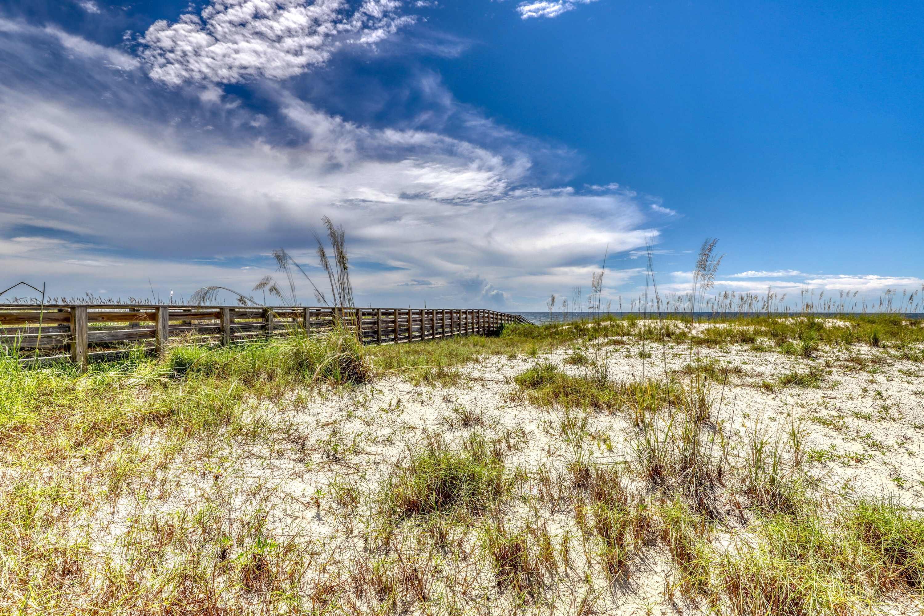 A sandy beach with a wooden fence and sparse vegetation.