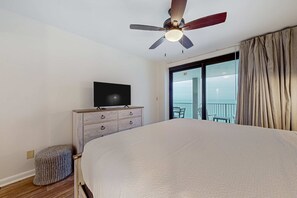 A bedroom with a bed, a TV on a wooden dresser, a ceiling fan, a balcony with a view, and a window with curtains. - Lovely resort condo with spectacular Gulf views, pool & tennis (Orange Beach)