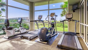 A gym with treadmills, stationary bikes, and ellipticals, large windows, and a view of greenery. - Beachfront Resort Condo Featuring Shared Hot Tub & Pool, Central AC, Free WiFi (Orange Beach)
