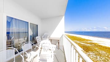 A balcony with white chairs and a table, overlooking a beach.