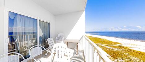 A balcony with white chairs and a table, overlooking a beach.