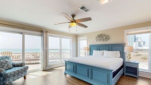 A bedroom with a large bed, a ceiling fan, a nightstand, and a view of the ocean.