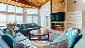 A spacious living room with a wooden ceiling, a large flat-screen TV, and a cozy seating area with a sofa and a coffee table.