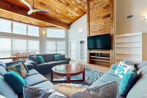 Ein geräumiges Wohnzimmer mit Holzbalkendecke, einem großen Flachbildfernseher und einer gemütlichen Sitzecke mit Sofa und Couchtisch.