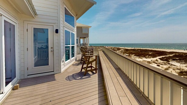 A wooden deck with a railing, a door, and a view of the beach.