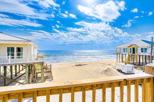 Une terrasse en bois située au bord de la plage, offrant une vue sur l’océan, et deux maisons de plage.