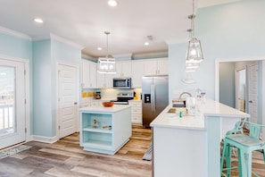 Une cuisine moderne avec des meubles blancs, un îlot central, des appareils en acier inoxydable et des chaises de couleur turquoise.