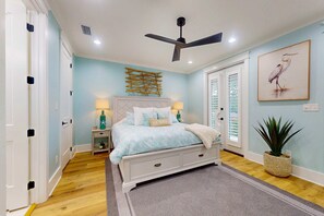 Ein Schlafzimmer mit Bett, Nachttischen, Deckenventilator, Wandbild und einer Topfpflanze.