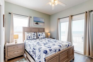 Ein Schlafzimmer mit Bett, Nachttischen, Deckenventilator, Fenster mit Vorhängen und Strand-Wandbild.