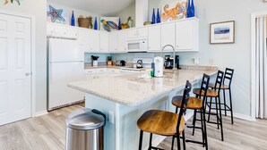 Cocina moderna con armarios blancos, encimera de granito, pileta de acero inoxidable y barra con taburetes.