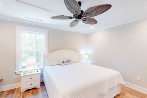 Ein Schlafzimmer mit einem Bett, einem Nachttisch, einem Fenster, einem Deckenventilator und einer Wandlampe.