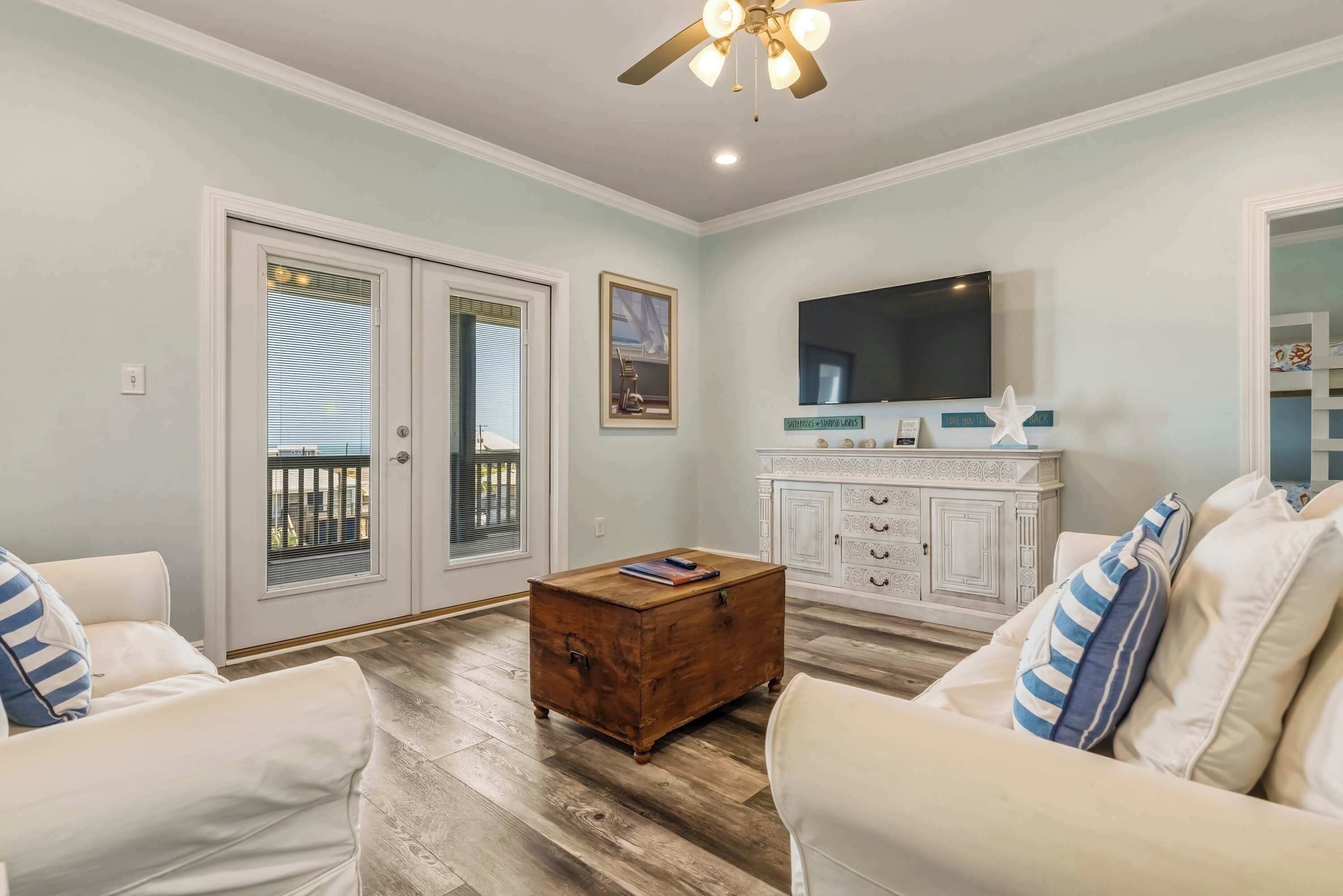 A living room with a wooden floor, white furniture, a ceiling fan, a television, and a cabinet.