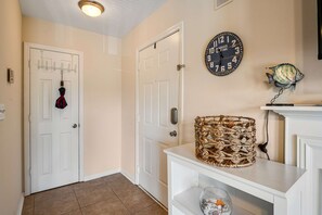 A hallway with a white door, a wall clock, a wicker basket, and a shelf with decorative items.