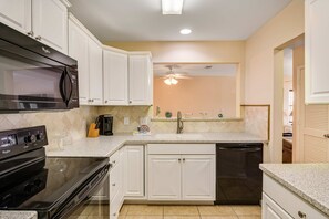 A kitchen with white cabinets, a black microwave, a stove, and a dishwasher.