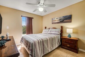 Ein Schlafzimmer mit einem Bett, einem Nachttisch mit Lampe, einem Deckenventilator und einem Bild an der Wand.
