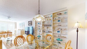 Een eetgedeelte met een glazen tafel en houten stoelen, omringd door witte planken met diverse decoratieve objecten.