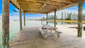 Een houten terras met een picknicktafel, houten pilaren en uitzicht op gebouwen aan de overkant van het water.