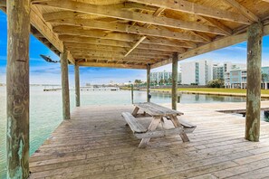 Eine Holzterrasse mit Picknicktisch, Holzsäulen und Blick auf Gebäude über dem Wasser.