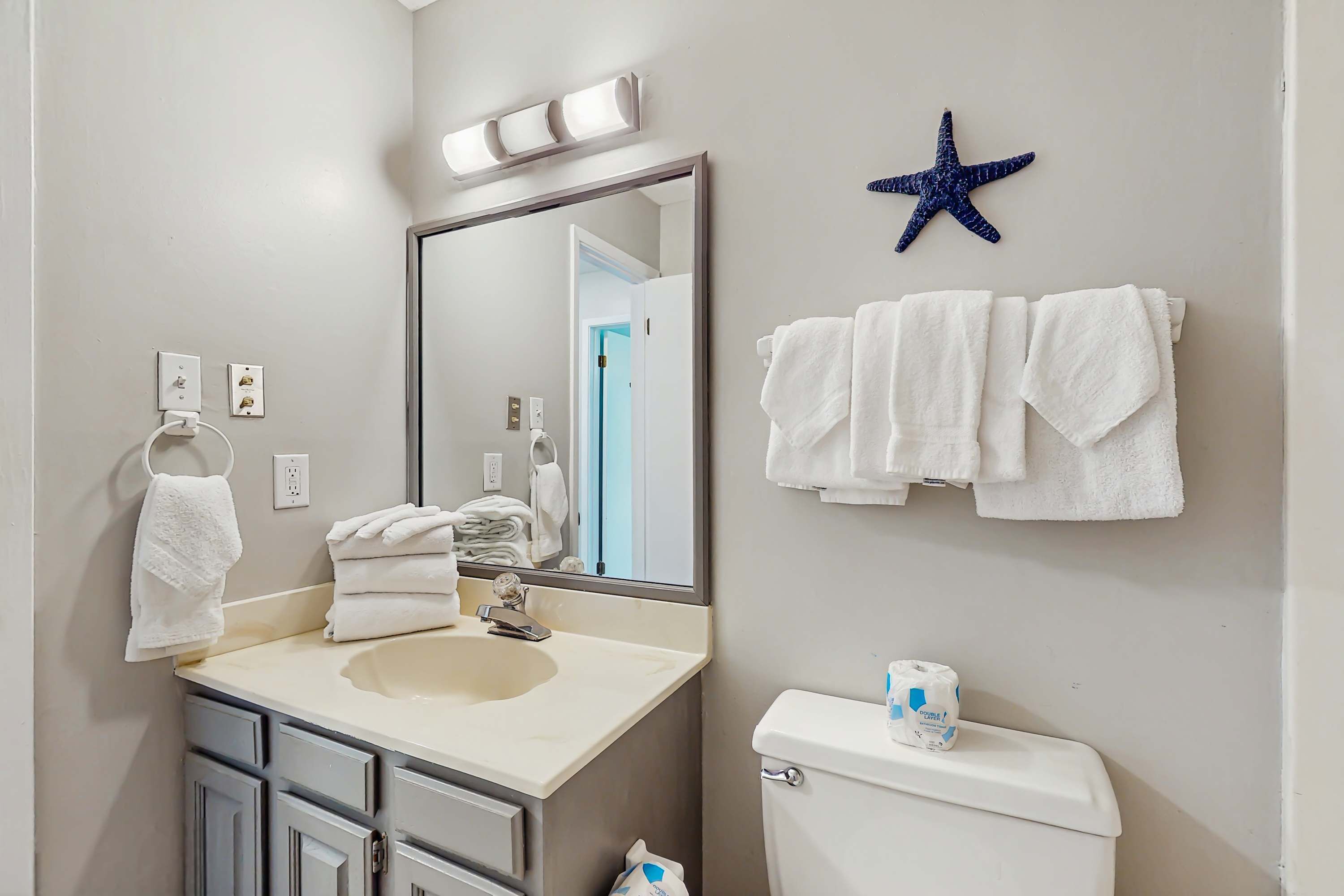 A bathroom with a sink, mirror, towels, toilet, and a starfish decoration.