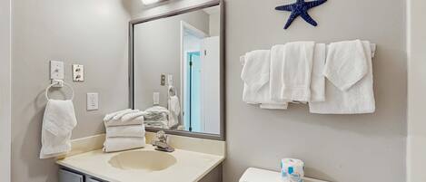 A bathroom with a sink, mirror, towels, toilet, and a starfish decoration.