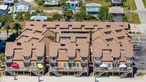 Een strandhotel met meerdere balkons, een overdekte doorgang en een zandstrand.