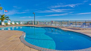 Une piscine avec une terrasse en bois, des chaises longues et un drapeau.