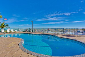 A swimming pool with a wooden deck, lounge chairs, and a flag. - Gulf-front condo with central AC, balcony & pool (Gulf Shores)