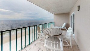 Un balcon avec vue sur l’océan, une table ronde et des chaises blanches.