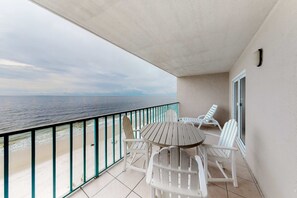 A balcony with a view of the ocean, a round table, and white chairs. - Gulf-front condo with central AC, balcony & pool (Gulf Shores)
